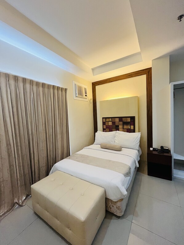 Una habitación de hotel con cama, mesita de noche, ventana con cortinas y puerta.