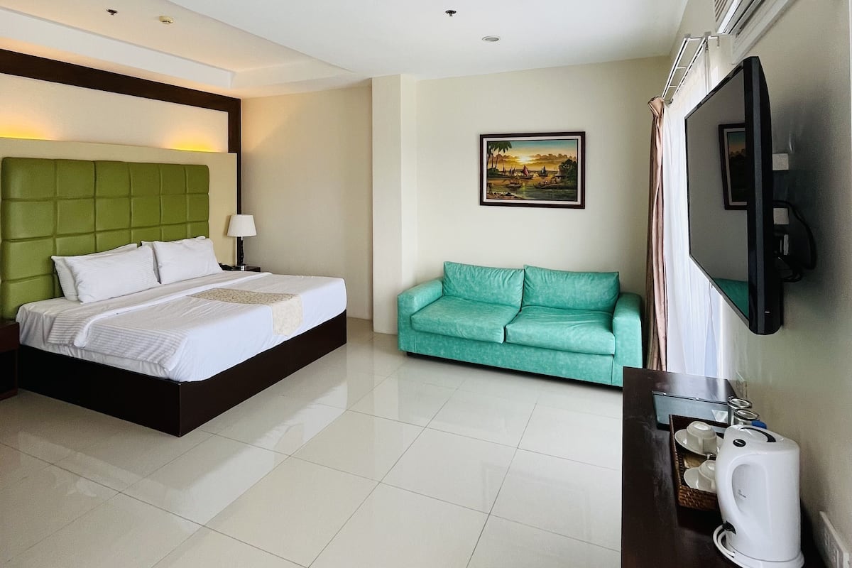 A hotel room with a bed, a green sofa, a TV, and a coffee maker.
