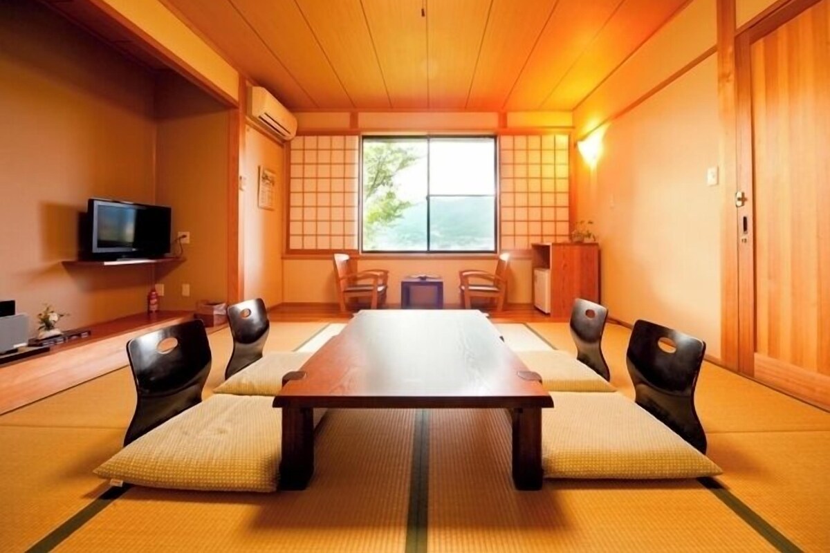 Una habitación japonesa tradicional con suelo de tatami, una mesita baja y un televisor en la pared.