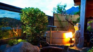 A hot spring bath area with a wooden structure, rocks, and a view of mountains.