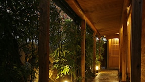 A wooden corridor with a tiled floor, surrounded by bamboo plants and a stone wall.
