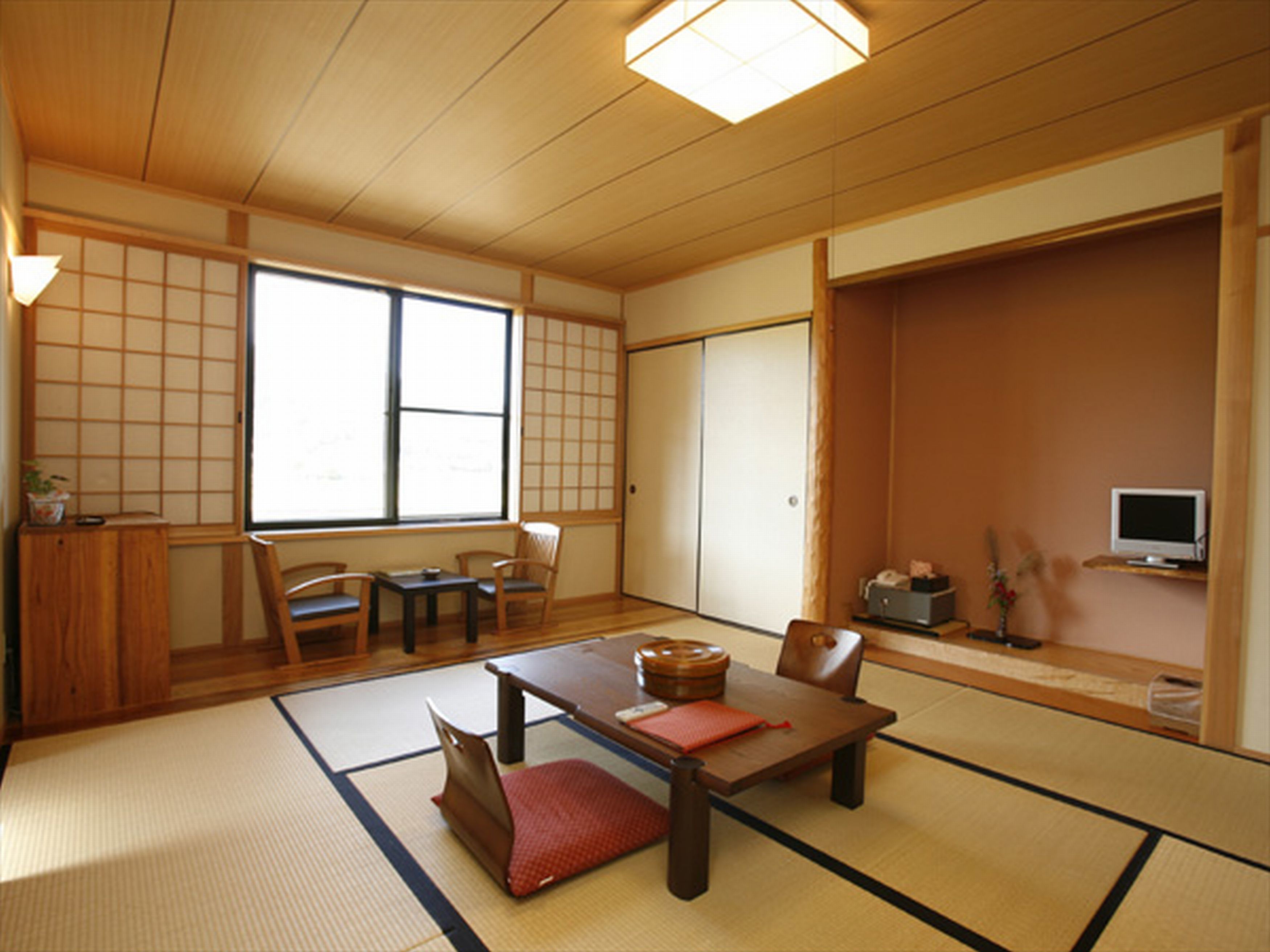 Ein traditioneller japanischer Raum mit Tatami-Böden, einem niedrigen Tisch, Stühlen, einer Schiebetür und einem Fernseher.