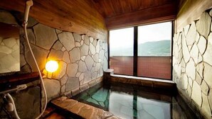 A stone-walled hot tub with a wooden ceiling and a view of the outdoors.
