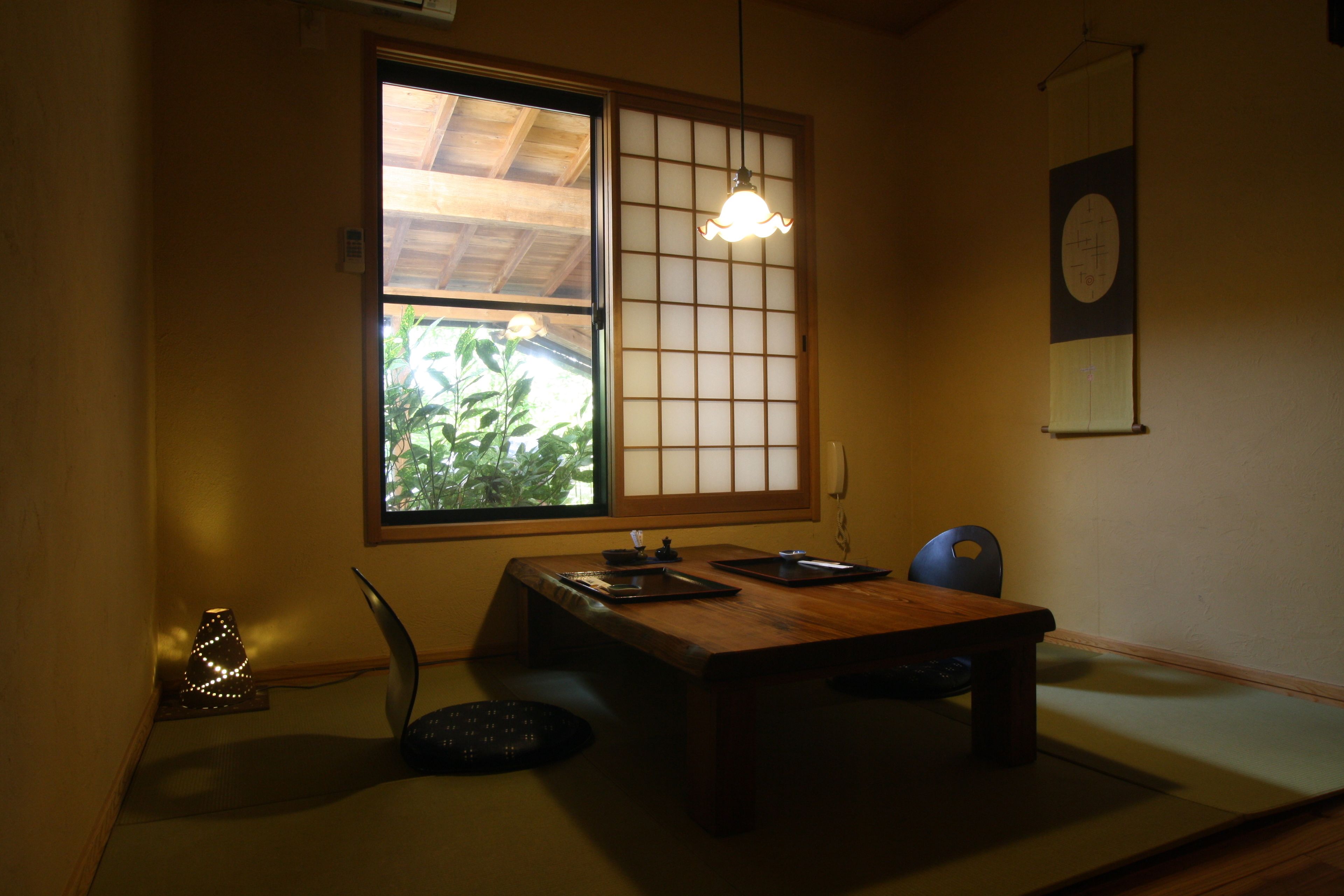 Una habitación japonesa tradicional con suelo de tatami, una mesa de madera baja, una lámpara colgante y una puerta corredera de shoji.