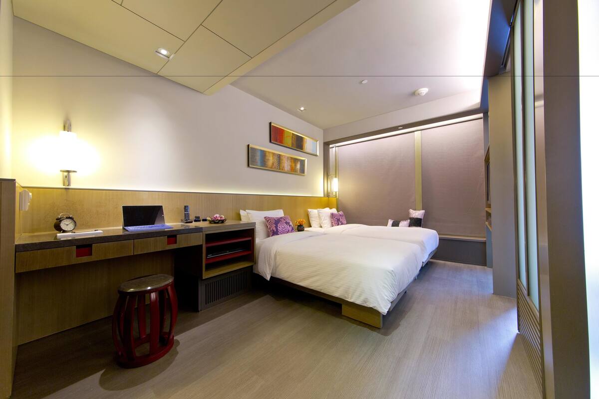 A modern hotel room with a bed, desk, and stool.