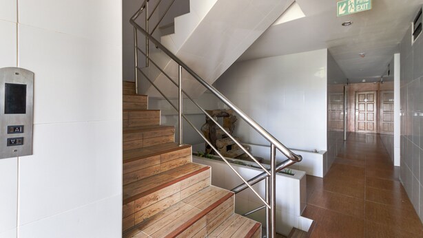 A modern staircase with wooden steps and metal railings, leading to a hallway with a fire exit sign.
