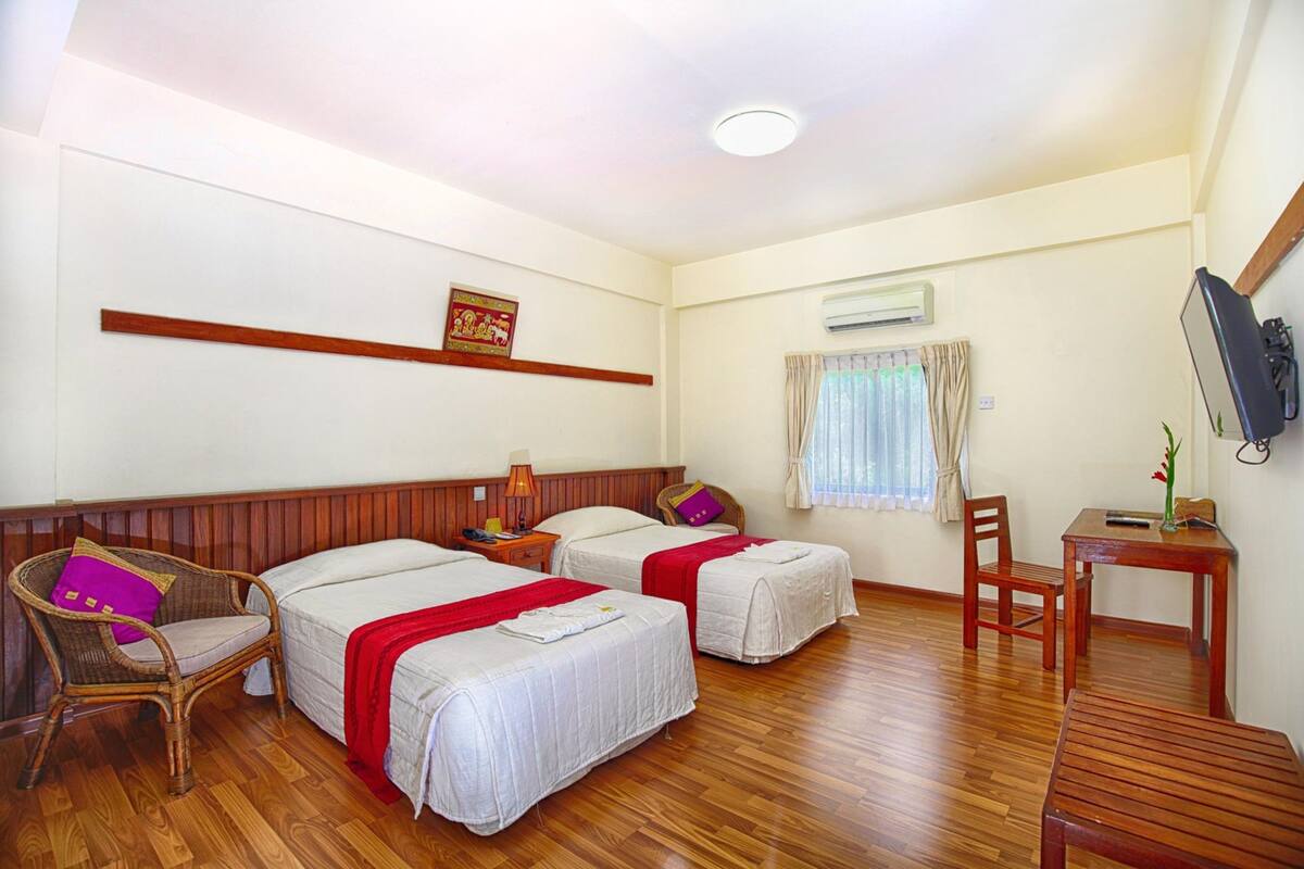 Habitación de hotel con dos camas, suelo de madera, televisor, una mesita y una ventana con cortinas.