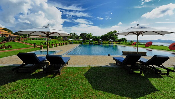 A pool area with lounge chairs and umbrellas, surrounded by greenery and a clear sky. - Sakura Inn (Nyaung-U)
