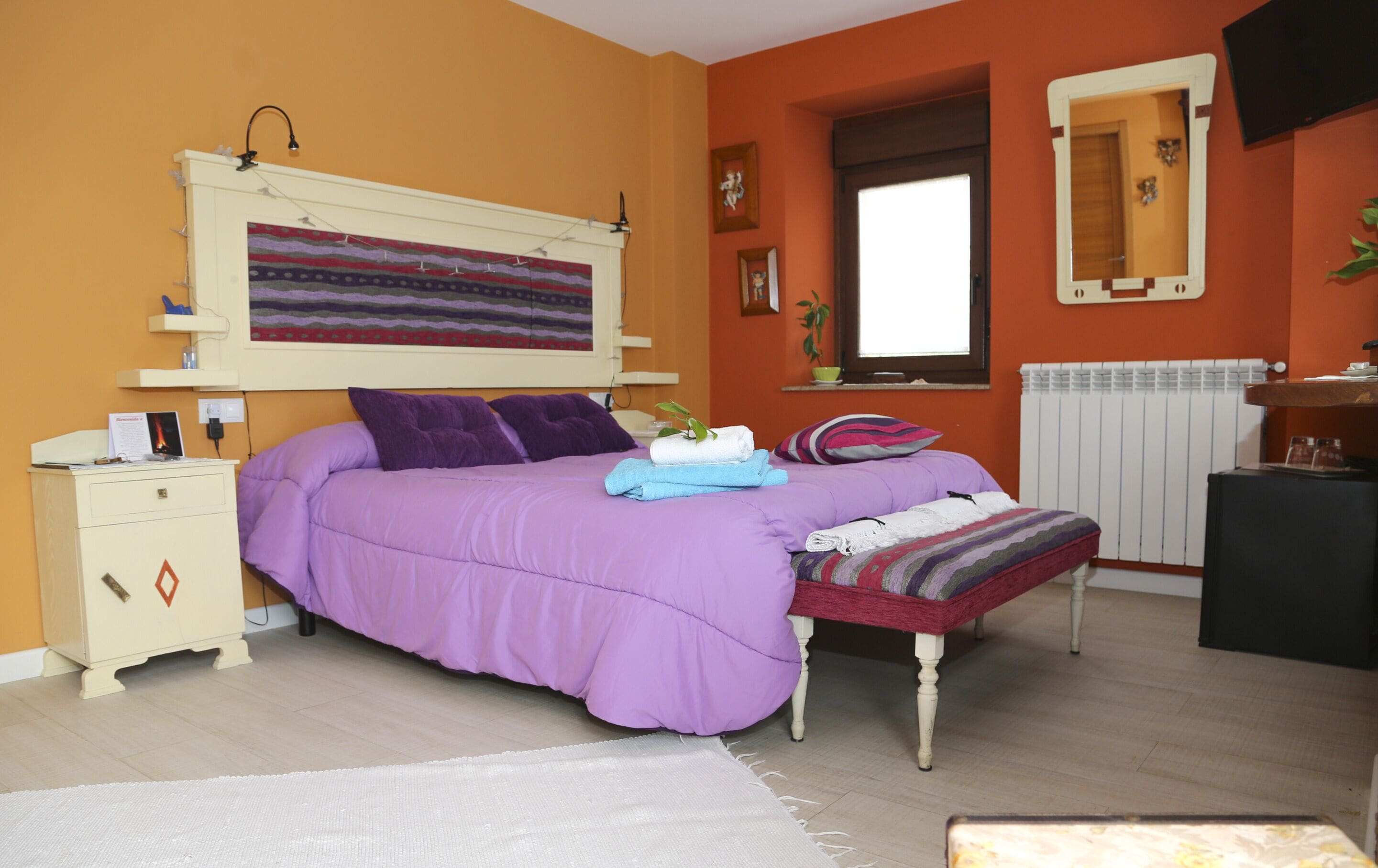 A bedroom with a bed, a nightstand, a dresser, a window, and a radiator.