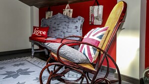 Una mecedora de mimbre con un cojín con la bandera Union Jack, un cojín rojo con la palabra 'Love' escrita y un cojín blanco con estampado floral.