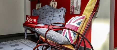 A wicker rocking chair with a Union Jack cushion, a red cushion with "Love" written on it, and a white cushion with a floral pattern.