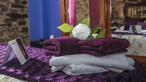 Una cama ordenada con toallas moradas y una flor blanca, un cartel y un espejo que refleja la habitación.