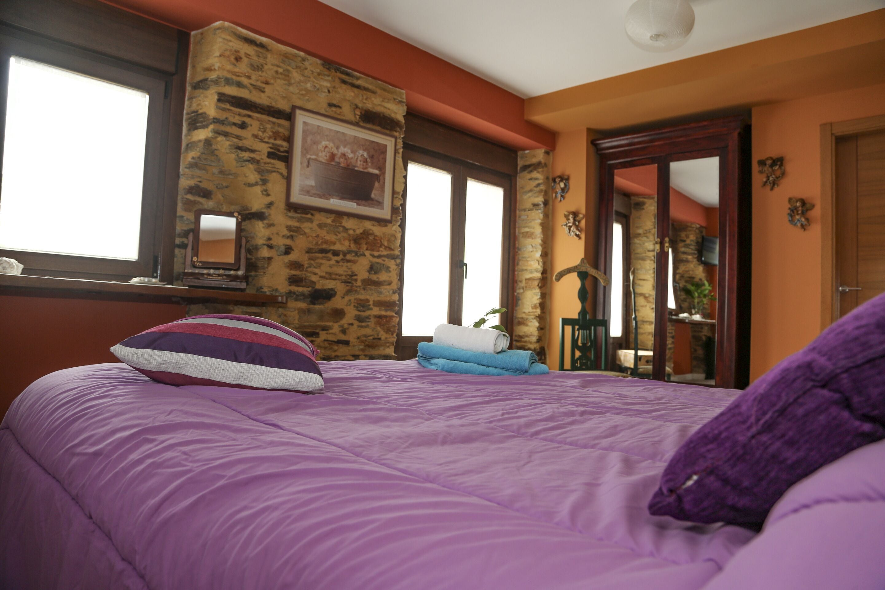 Un dormitorio con colcha morada, pared de piedra y puerta de madera.