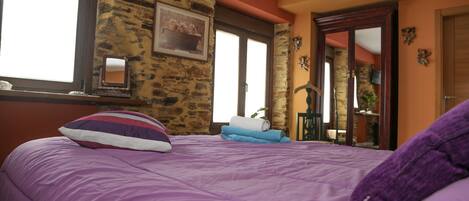 Un dormitorio con colcha morada, pared de piedra y puerta de madera.