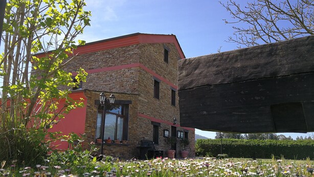Un edificio de piedra con techo rojo y un pequeño porche adornado con plantas en macetas.