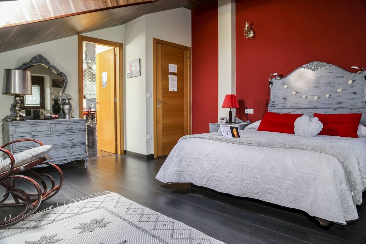 Une chambre à coucher avec un lit, une commode, un miroir et un mur rouge.