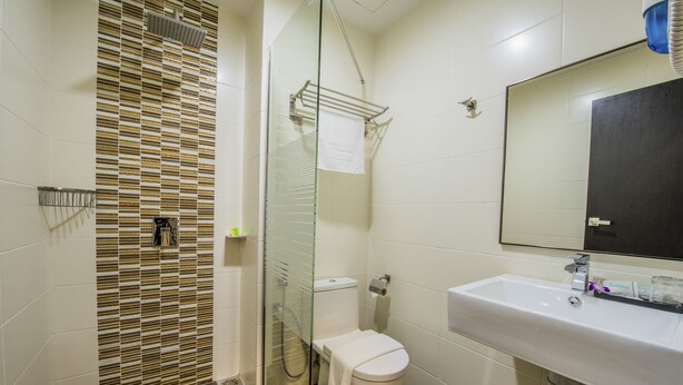 Une salle de bain avec une douche à parois de verre, des toilettes blanches, un lavabo avec un miroir et un sol carrelé.