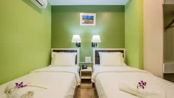 Habitación de hotel con dos camas, paredes verdes, una mesita con una lámpara y un cuadro en la pared.