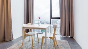 A modern room with a table and two chairs, large windows with curtains, and a view of a cityscape. - Luzzeri Suite Empire Damansara (Petaling Jaya)