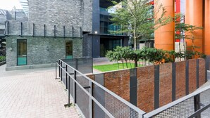 A modern building with a brick facade, a metal fence, and a small garden area. - Luzzeri Suite Empire Damansara (Petaling Jaya)