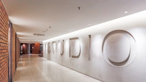 A modern hallway with a brick wall on one side and a white wall with circular cutouts spelling out "STUDIO". - Luzzeri Suite Empire Damansara (Petaling Jaya)