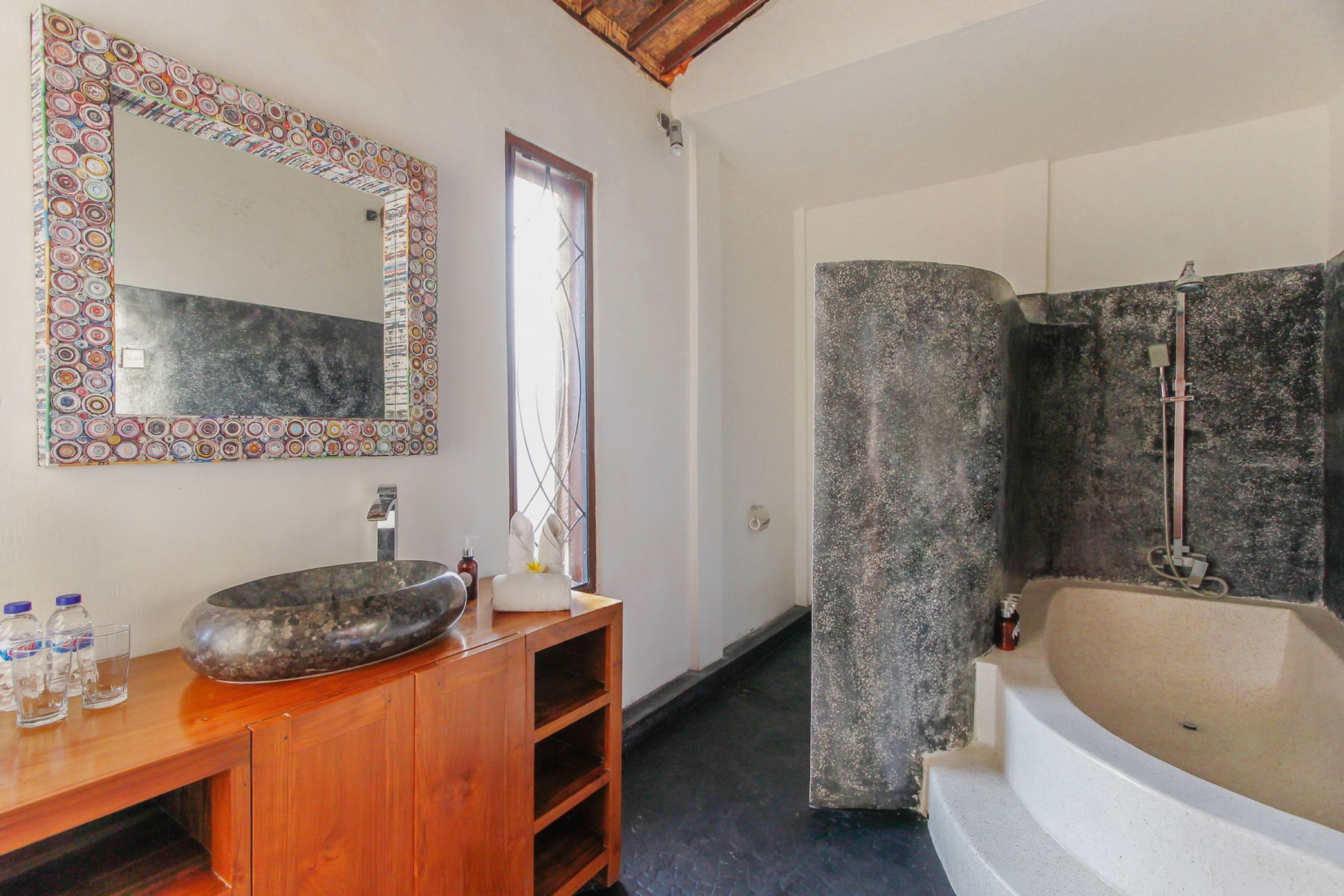 Un baño con una bañera grande, un tocador de madera con lavamanos de piedra y un espejo con marco decorativo.