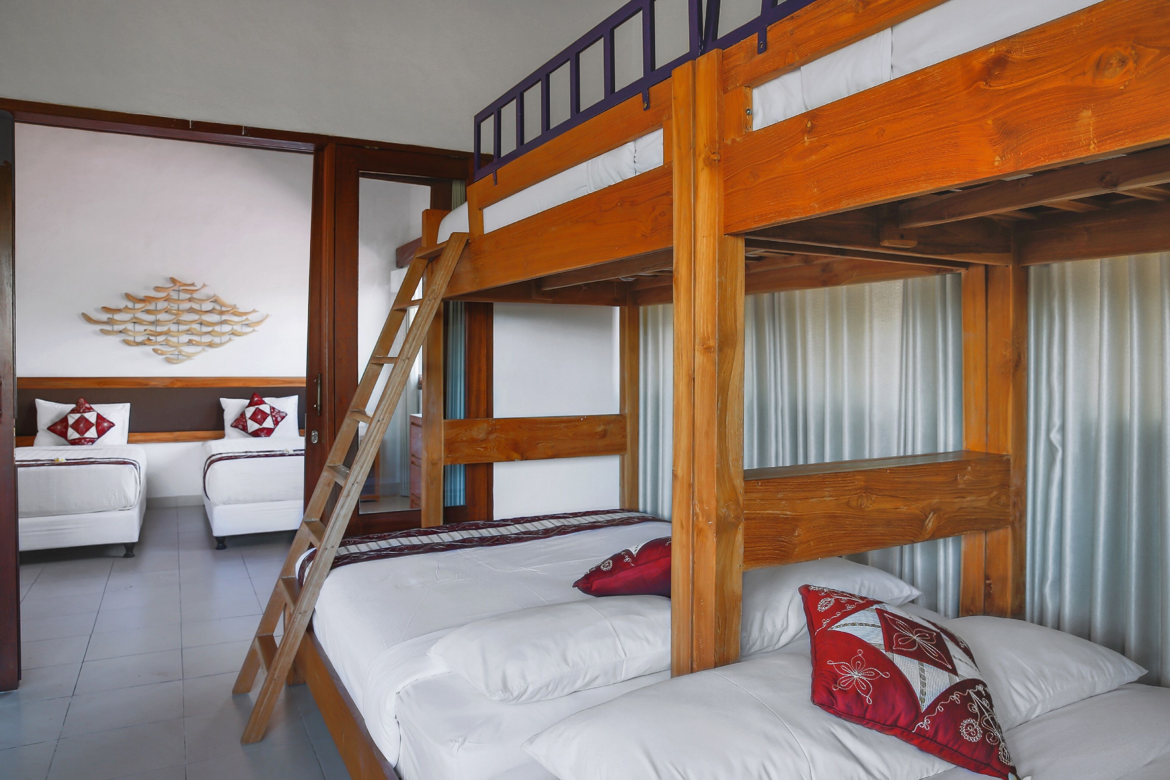 A bunk bed with a wooden ladder, white bedding, and red decorative pillows.