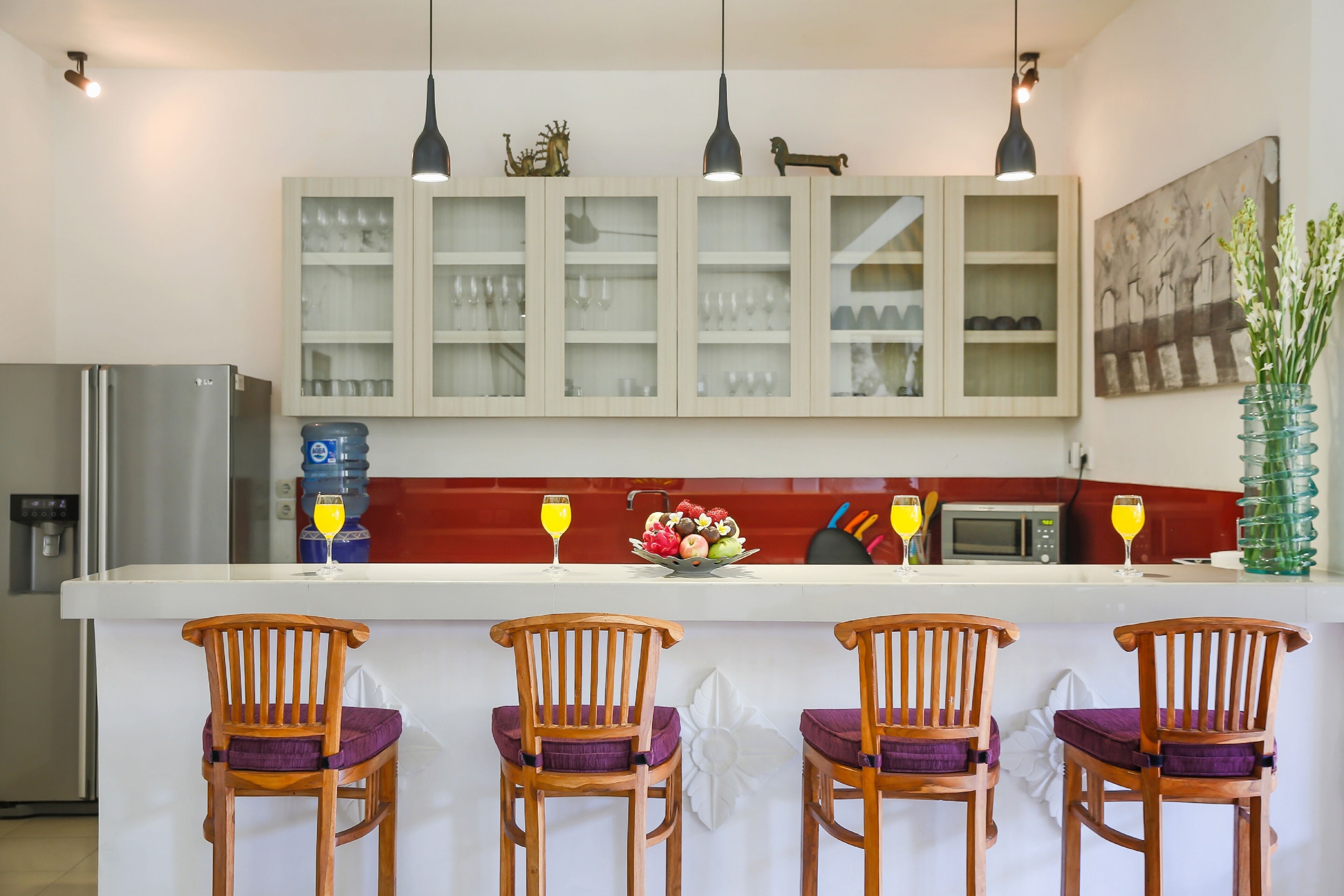 A kitchen with a central island, wooden chairs, a refrigerator, cabinets, and a microwave.