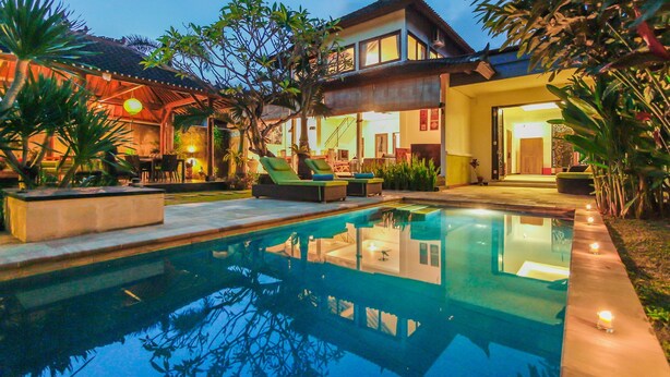 A pool area with a house in the background, surrounded by tropical plants. - Villa Bali Caviar (Seminyak)