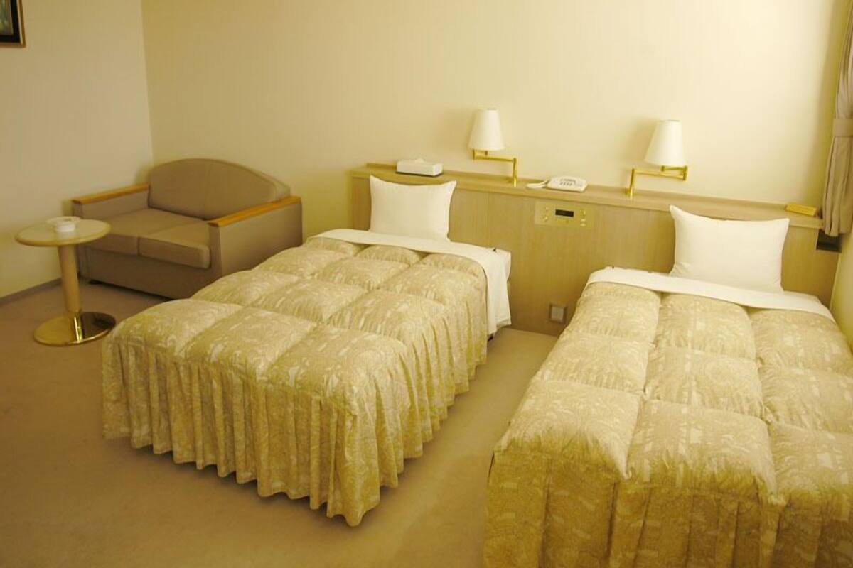 A hotel room with two beds, a small round table, a sofa, and a nightstand with a lamp.