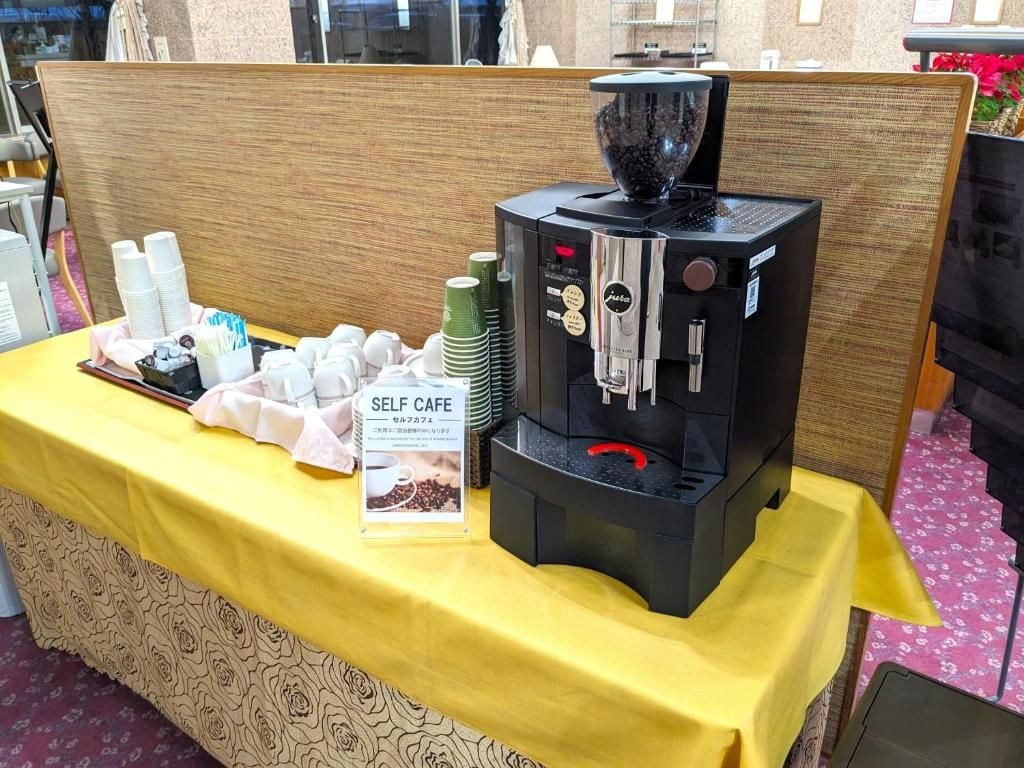 Una estación de café autoservicio con una máquina de café, tazas y un cartel.