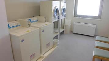 Een wasserette met vier wasmachines, een radiator en een raam.