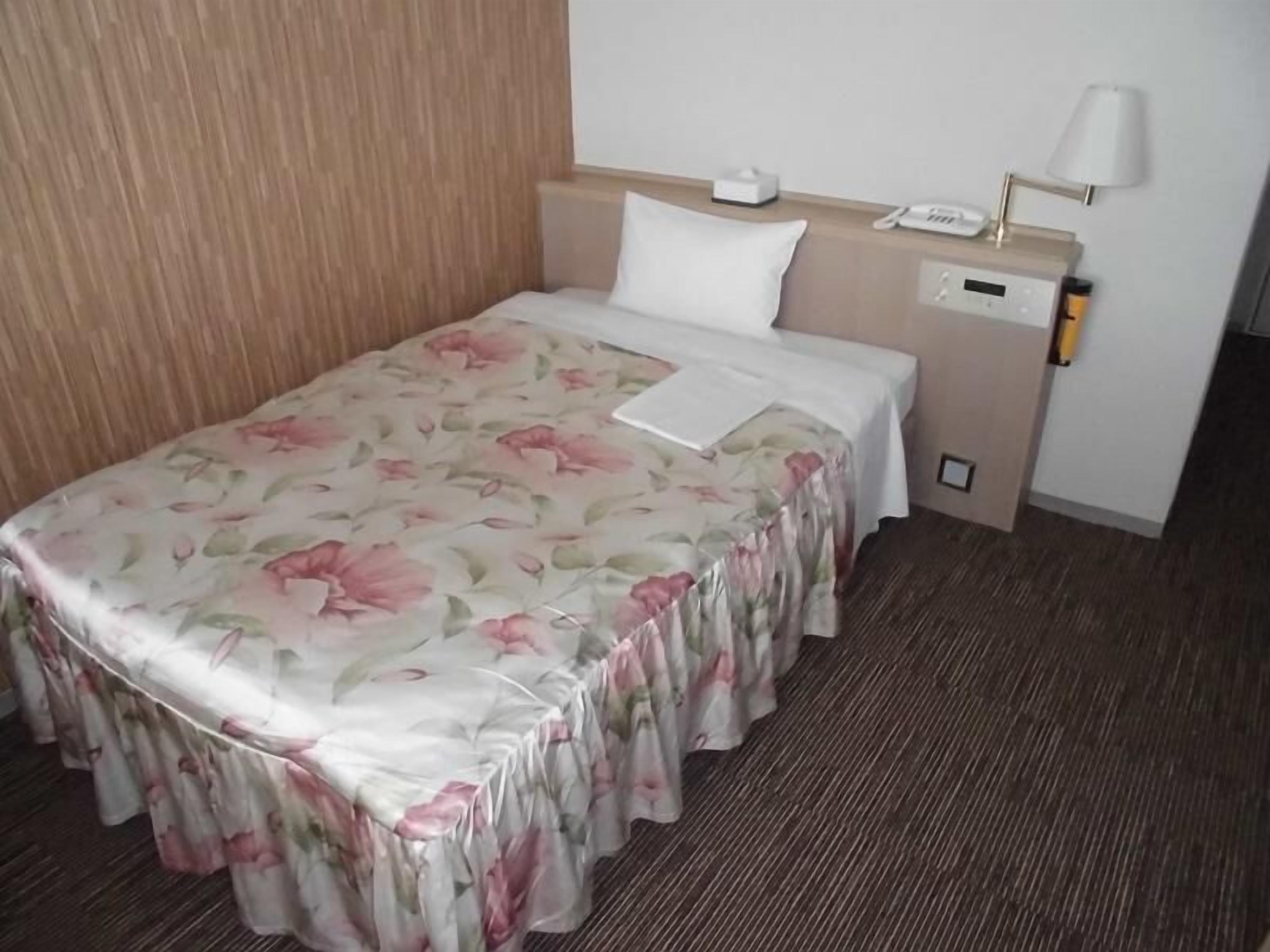 Habitación de hotel con colcha estampada, mesita de noche con lámpara, teléfono y una pequeña mesita.