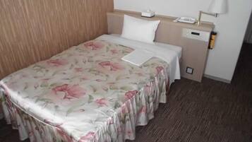 Habitación de hotel con colcha estampada, mesita de noche con lámpara, teléfono y una pequeña mesita.