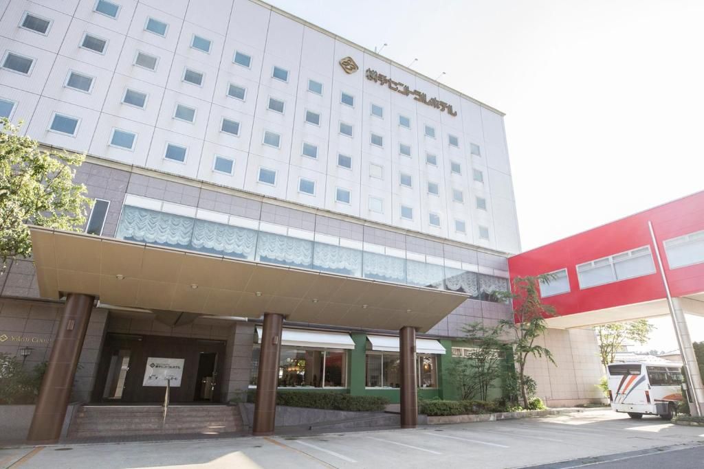 Un hotel de varios pisos con fachada moderna, un acceso cubierto y un estacionamiento con un autobús.
