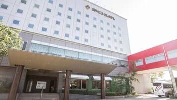 Un hotel de varios pisos con fachada moderna, un acceso cubierto y un estacionamiento con un autobús.