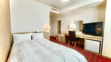 A hotel room with a bed, desk, chair, television, and a small refrigerator.
