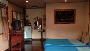 Una habitación con piso de madera, una cama con ropa de cama azul, un televisor y una pequeña mesa.