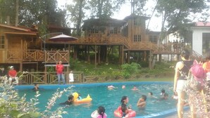 A swimming pool area with wooden deck structures and a person standing on the deck. - Borneo Tree House (Kota Kinabalu)