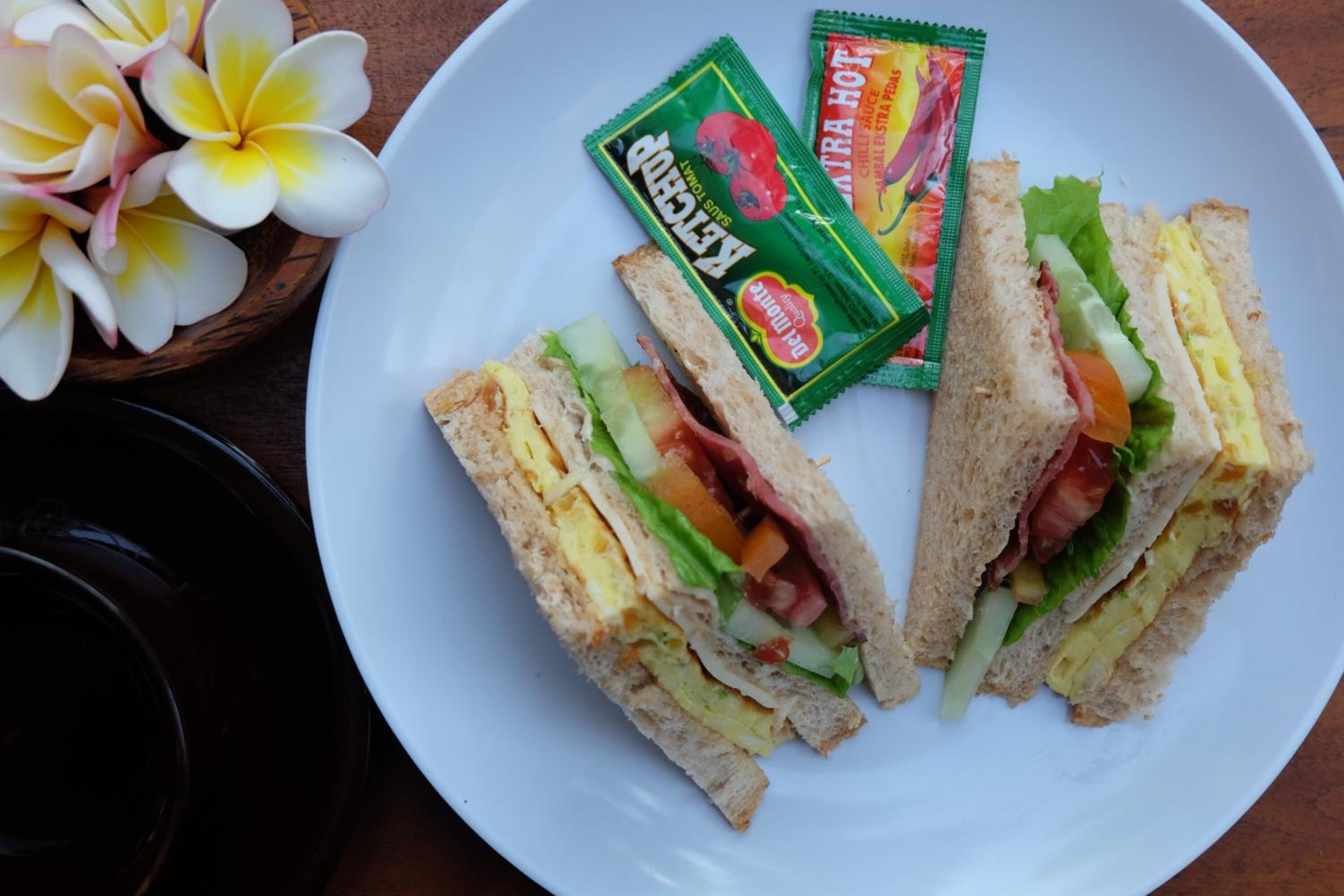 A plate with three sandwiches and two packets of condiments.