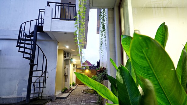 A narrow alleyway with a spiral staircase leading to a balcony, surrounded by lush greenery and a cobblestone path. - D'Pande (Kuta)