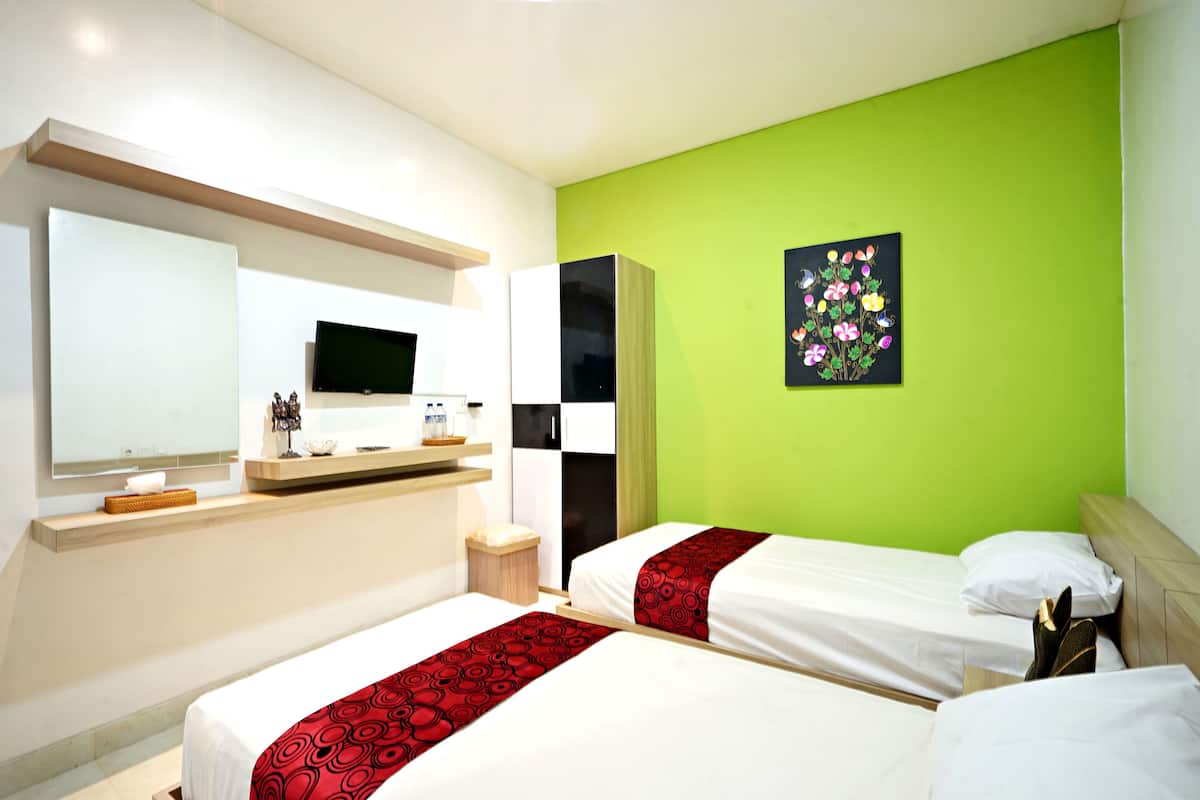 Habitación de hotel con dos camas, televisión, espejo y pared verde.