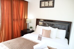 A hotel room with a large bed, a nightstand with a lamp and a small plant, and a framed picture on the wall. - Sea Pearl Manila Suites (Manila)