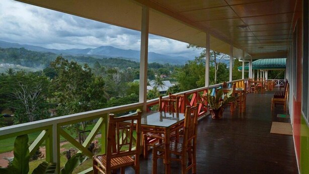 Un espacio de estar al aire libre techado con mesas y sillas, con vistas a un paisaje montañoso.