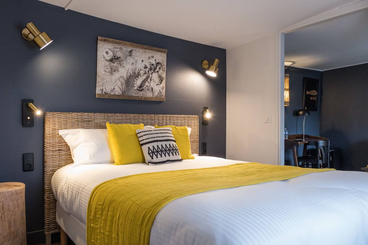 A neatly made bed with a yellow throw blanket, a headboard with a woven design, and a wall-mounted artwork above it.