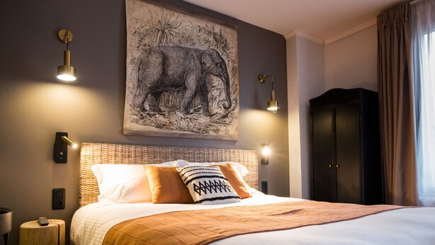 Ein ordentlich bezogenes Bett mit einem gemusterten Überwurf, ein großes Elefantenbild an der Wand und ein Kleiderschrank.