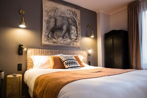 Ein ordentlich bezogenes Bett mit einem gemusterten Überwurf, ein großes Elefantenbild an der Wand und ein Kleiderschrank.