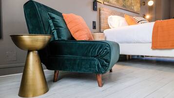 A modern bedroom with a green velvet armchair, a brass side table, and a white bed with orange and white pillows.