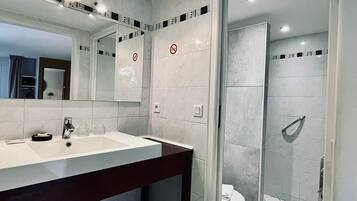 Un baño moderno con un espejo grande, un lavabo blanco y una ducha con mampara de vidrio.