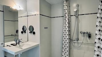 Un bagno con un lavandino bianco, uno specchio, una doccia con tenda decorata e un pavimento piastrellato.